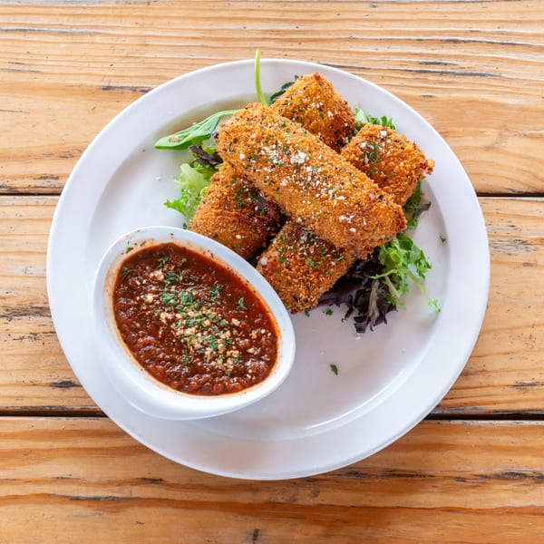 Crispy fried mozzarella sticks with marinara sauce and fresh greens on a white plate.