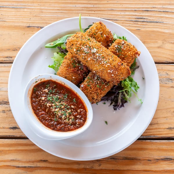 Crispy fried mozzarella sticks with marinara sauce and fresh greens on a white plate.