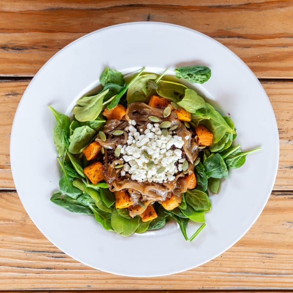 A vibrant salad with spinach, roasted butternut squash, caramelized onions, feta cheese, and pumpkin seeds.