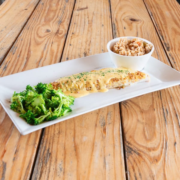 Breaded fish fillet with creamy sauce, broccoli, and rice on a white plate over a wooden table.