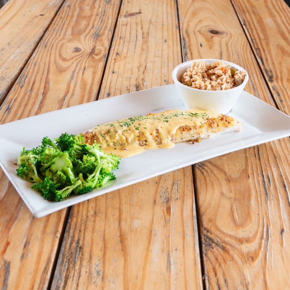 Breaded fish fillet with creamy sauce, broccoli, and rice on a white plate over a wooden table.