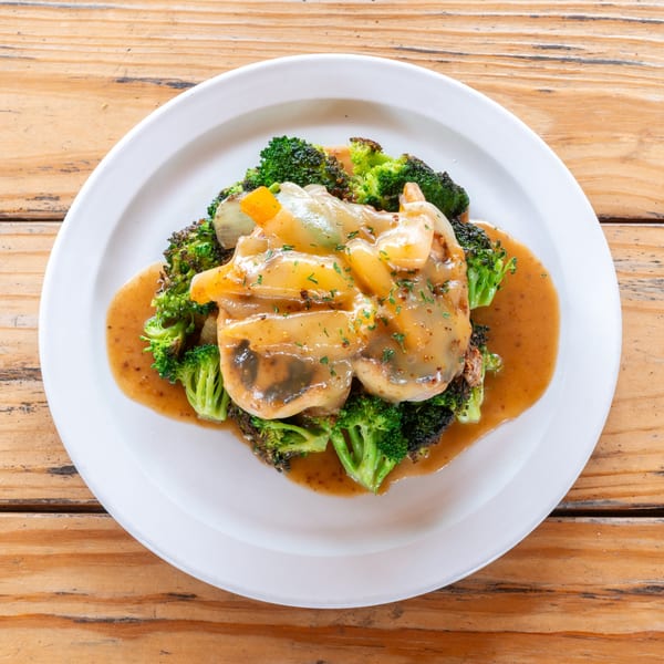 Chicken and broccoli dish with a savory sauce, served on a white plate on a wooden table.
