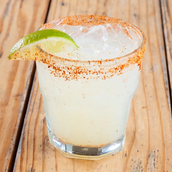 A margarita with a chili-salt rim and a lime wedge, on a rustic wooden table.