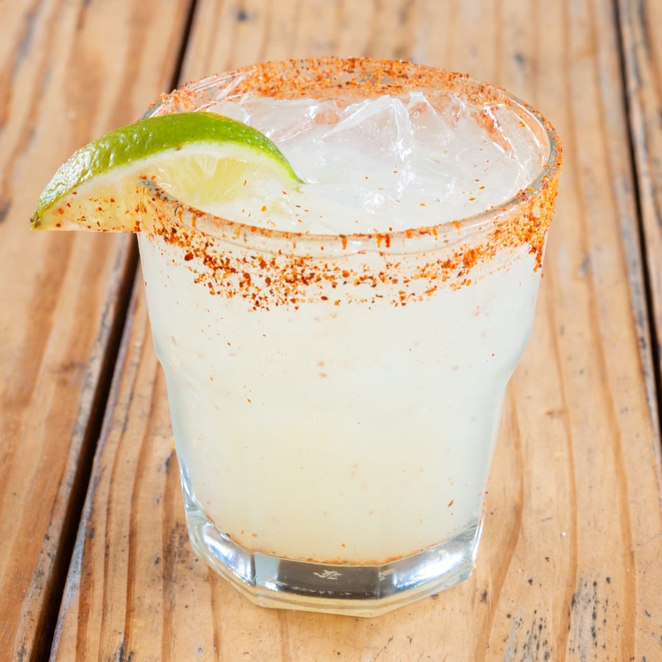 A margarita with a chili-salt rim and a lime wedge, on a rustic wooden table.