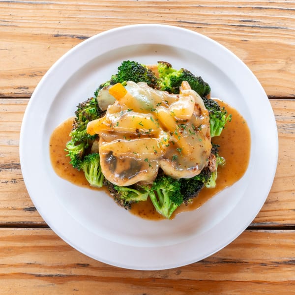 Chicken and broccoli covered in a rich brown sauce with onions and peppers on a white plate.