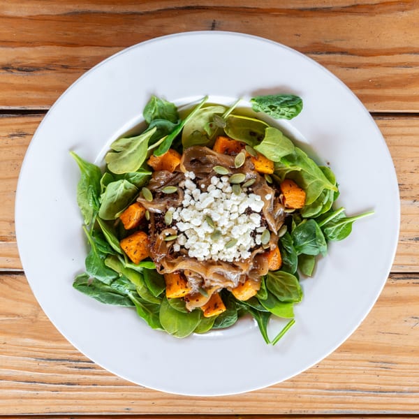 Spinach salad with roasted butternut squash, caramelized onions, feta cheese, and pumpkin seeds.